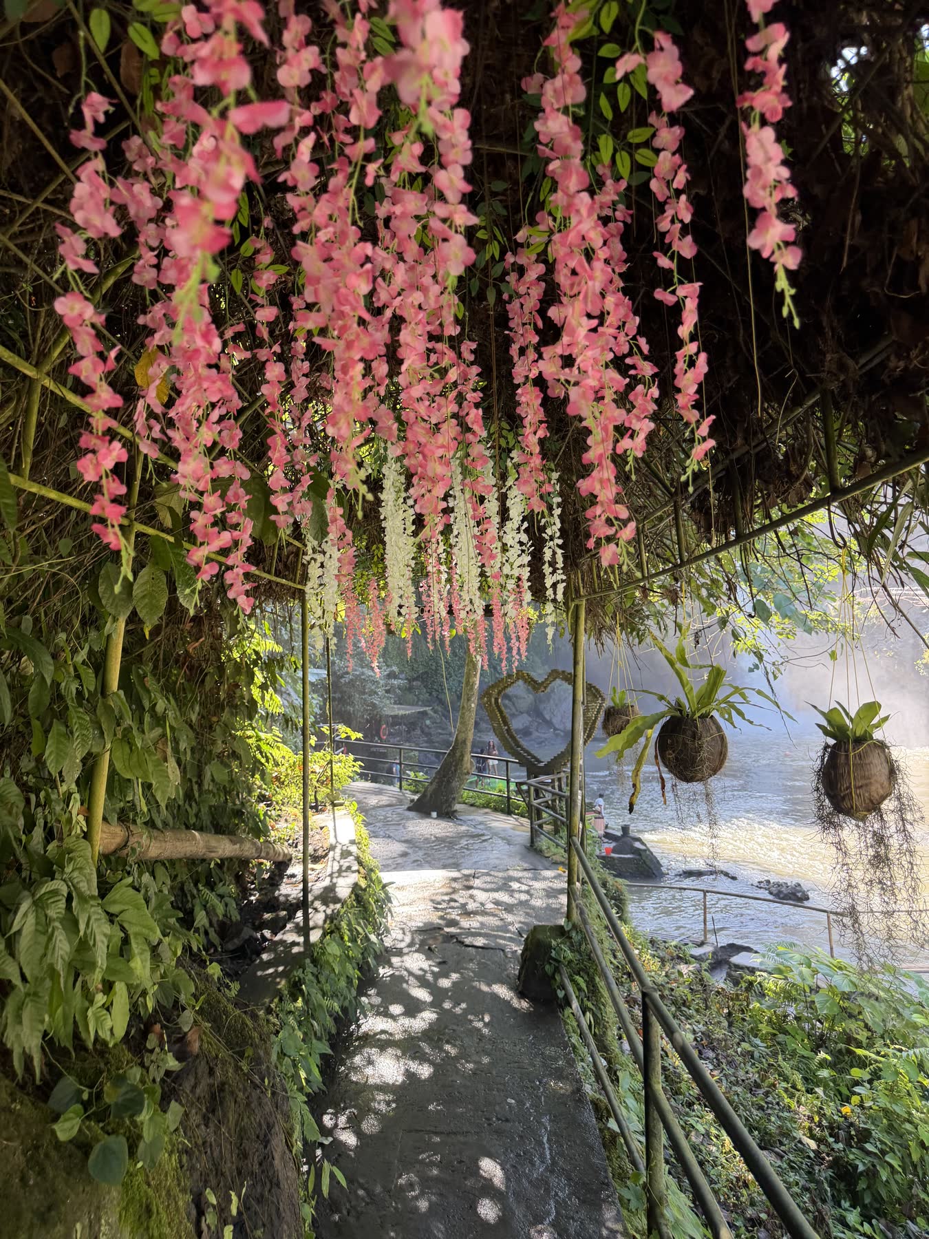 Weg durch einen Bogen aus rosa Blüten hinunter zu einem Fluss